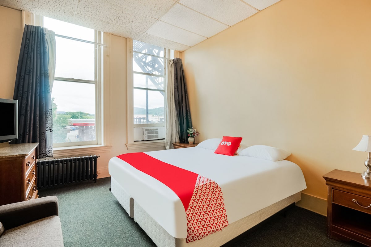 Una habitación de hotel con cama, cómoda, televisor y ventana con cortinas.