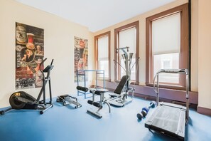 A gym with exercise equipment, posters on the wall, and large windows.