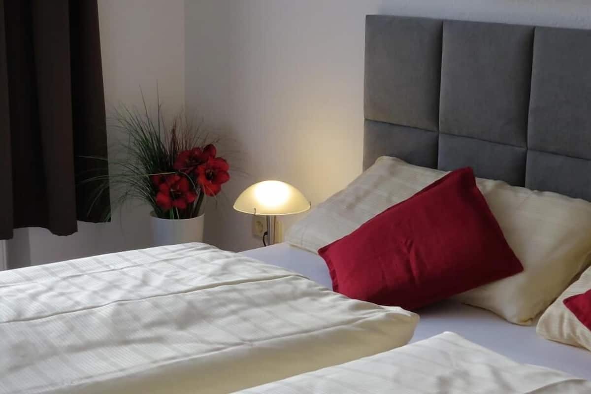 Camera d'albergo con un letto, un comodino, una lampada e un vaso con fiori.