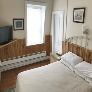 A bedroom with a bed, a television, a window with blinds, a door, and a framed picture on the wall.
