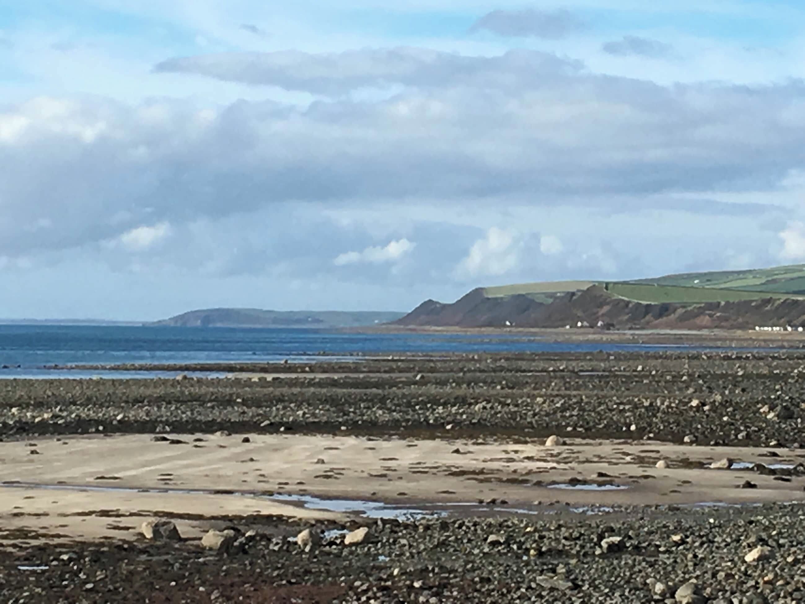Ein felsiger Strand mit Blick auf das Meer und ferne Hügel.
