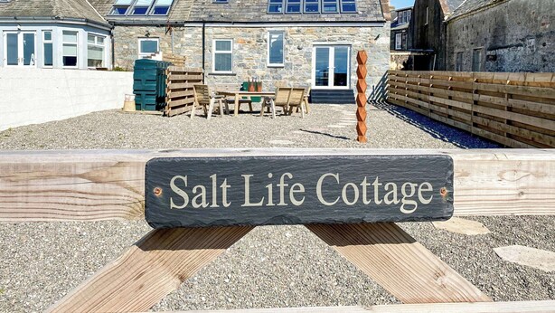 Kivinen mökki, jonka yläpuolella on kyltti, jossa lukee: ”Salt Life Cottage”.