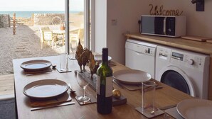 Ruokapöytä, jossa on neljälle katettu paikka: lautaset, aterimet ja viinilasit, ja pöydältä avautuu näkymä rannalle.
