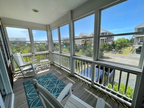 A covered porch with white railings, a blue patterned rug, and two white chairs.