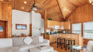 Ein gemütliches Blockhausschlafzimmer mit Holzbalkendecke, einem Wohnbereich mit Sofa und Couchtisch, einer Küche mit Holzschränken und einem Essbereich mit Tisch und Stühlen.
