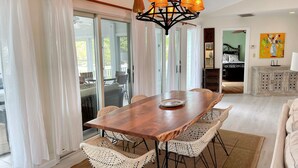 Uma sala de jantar com mesa de madeira, cadeiras de vime branco e um candelabro.