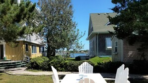 A patio with white Adirondack chairs and a table, surrounded by a well-maintained lawn and a large tree. - Bragg-Tolson House (Formerly Serendipity): Historic Home with Modern Convenience (Ocracoke)