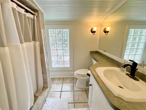 Ein Badezimmer mit einer weißen Badewanne, einer Toilette und einem Fenster mit Verzierglas.