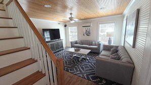 A living room with a staircase, a television, a sofa, and a patterned rug. - Bragg-Tolson House (Formerly Serendipity): Historic Home with Modern Convenience (Ocracoke)
