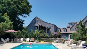 A swimming pool with lounge chairs and a beach ball, surrounded by a wooden fence and trees.