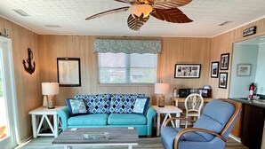 A living room with a teal sofa, a wooden coffee table, a blue armchair, and a ceiling fan. - Contentment: Spacious home, den, screened porch, marsh views. (Ocracoke)