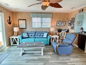 A living room with a teal sofa, a wooden coffee table, a blue armchair, and a ceiling fan.