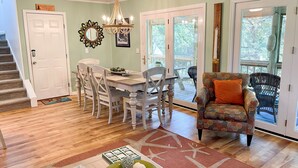 A dining area with a wooden table and chairs, a chandelier, and a sign reading "Portsmouth Village". - Contentment: Spacious home, den, screened porch, marsh views. (Ocracoke)