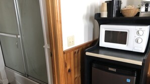 Une cuisine compacte équipée d’un four à micro-ondes et d’un petit réfrigérateur, avec un lambris en bois et une porte de douche en verre.