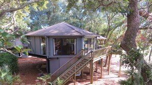 A house with a deck and a staircase leading up to it, surrounded by trees and greenery.