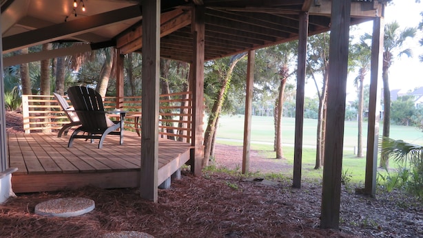 A wooden deck with a covered area, a lounge chair, and a view of a golf course.