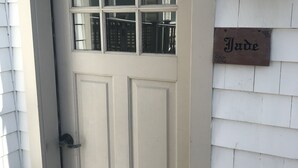 Une porte d’entrée de couleur beige, avec une fenêtre au-dessus, et une enseigne portant le nom « Jade » fixée au mur, sur le côté droit.