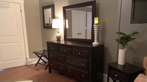 Une chambre avec une commode en bois, un miroir, une table de chevet avec une lampe, une chaise et une plante en pot.