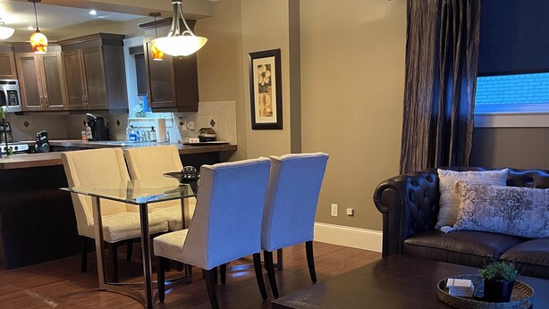 Un salon moderne avec une table basse marron foncé, deux fauteuils beiges, un canapé en cuir et un coin repas comprenant une table et des chaises en verre.