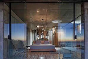 Une chambre moderne avec un grand lit, des murs en verre et une vue sur un escalier.