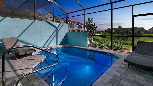 A swimming pool with a glass enclosure, lounge chairs, and a view of residential buildings.