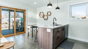 A modern kitchen with a central island, pendant lights, and a view through a sliding glass door. - Colorado Modern Cabin (Fort Collins)