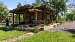 A wooden cabin with a covered porch, a dining area, and a garden with stone planters. - Colorado Modern Cabin (Fort Collins)