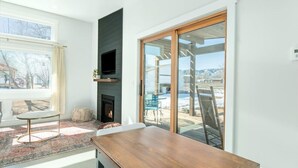 A room with a fireplace, a television mounted on the wall, a dining table, and a view of the outdoors through large sliding glass doors. - Colorado Modern Cabin (Fort Collins)