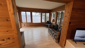 A cabin with a wooden interior, a plaid sofa, a chair, and a TV on a stand. - Sunset Beach - Log Home on Beautiful Indian Lake (Manistique)