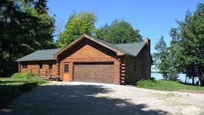 A log cabin with a large garage and a gravel driveway. - Sunset Beach - Log Home on Beautiful Indian Lake (Manistique)