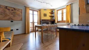 A cozy room with a wooden dining table, chairs, and a sofa. A large map is on the wall, and there's a fireplace with a mantel. - Meralda 2 SCOIATTOLO (Valfurva)