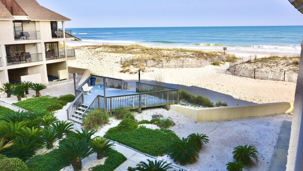 Un hotel frente a la playa con piscina, mobiliario exterior y vistas al océano.
