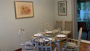 Un coin repas avec une table ronde en verre, des chaises en osier et un lustre.