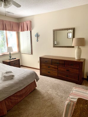 Quarto com cama, penteadeira, mesa de cabeceira, abajur e janela com persianas.