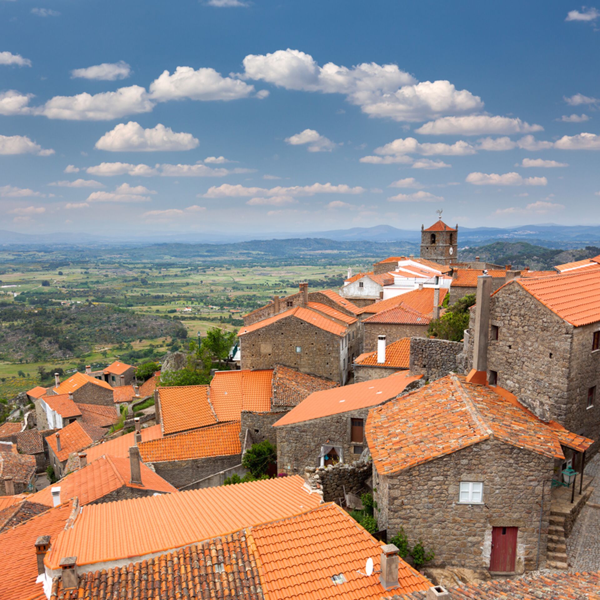 Une ville historique aux bâtiments en pierre et aux toits de tuiles rouges, qui se distingue par une tour imposante et offre une vue sur la campagne environnante.