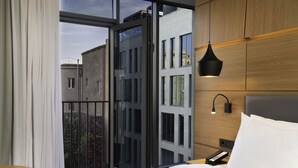 Ein modernes Hotelzimmer mit großem Fenster, einem Bett, einem Nachttisch und einer Wandlampe.