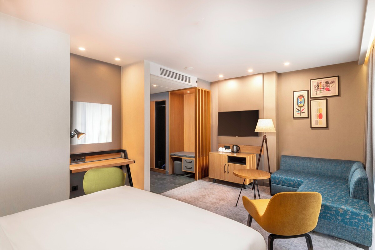 Een hotelkamer met een bed, bureau, stoel, televisie en bank.