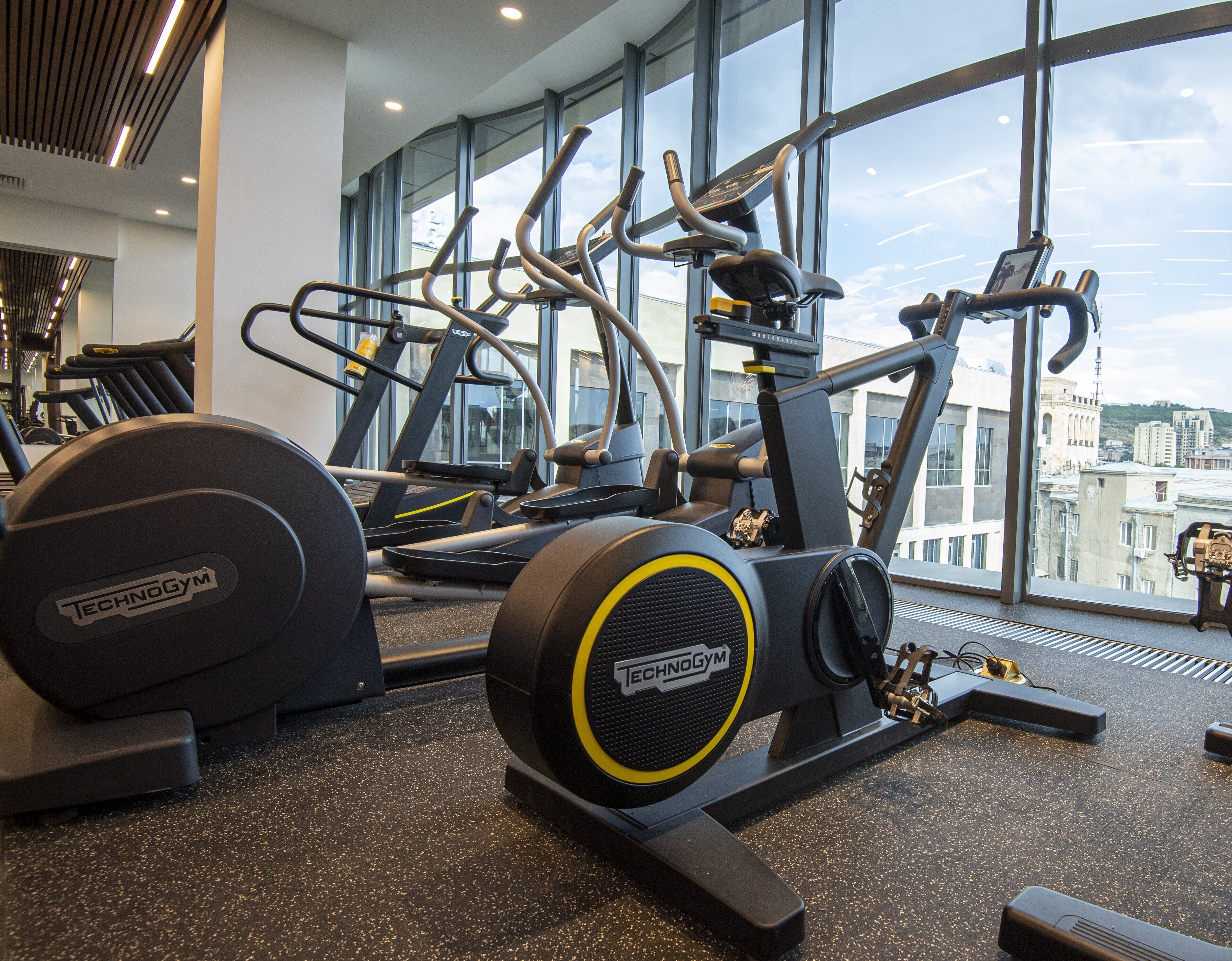 A gym with Technogym equipment, large windows, and a city view.