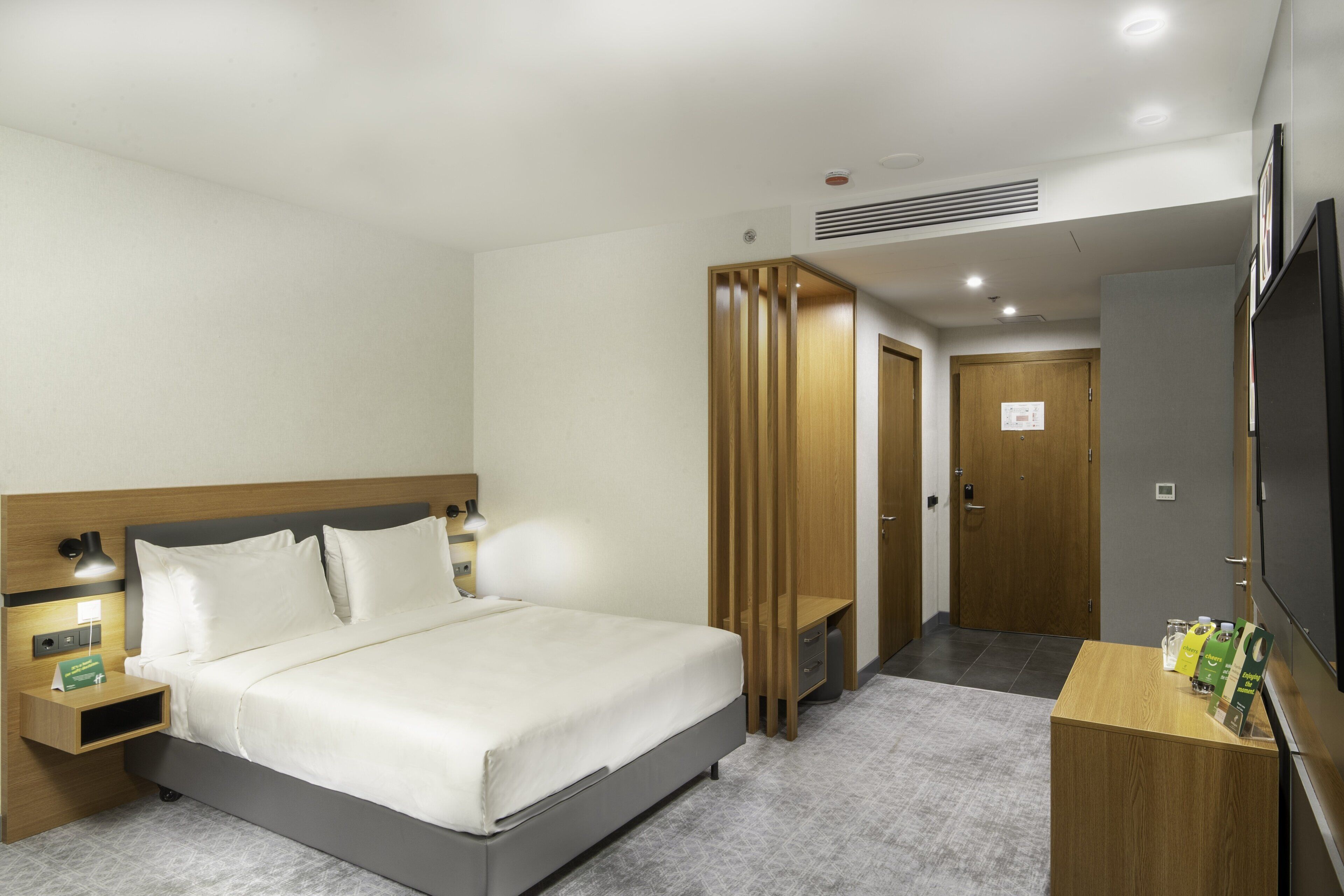 Une chambre d’hôtel comprenant un lit, des tables de chevet, un téléviseur, une armoire en bois et un bureau avec une chaise.