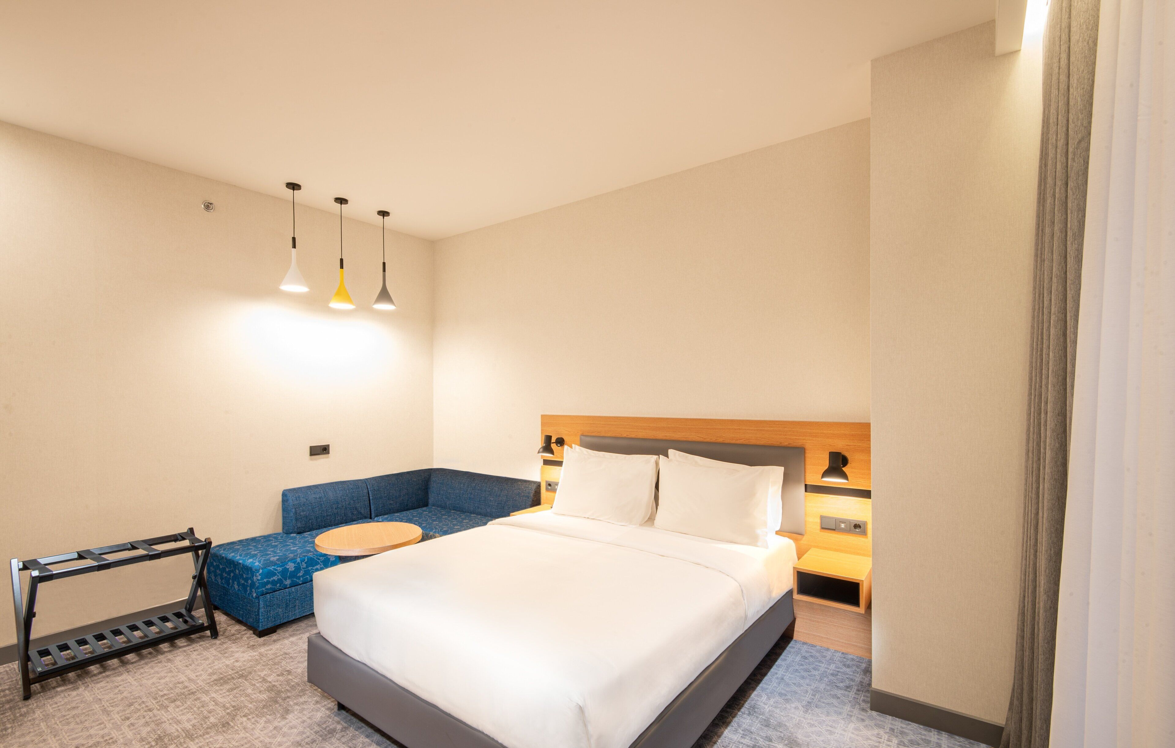 A hotel room with a bed, a blue sofa, a small table, and a hanging light fixture.