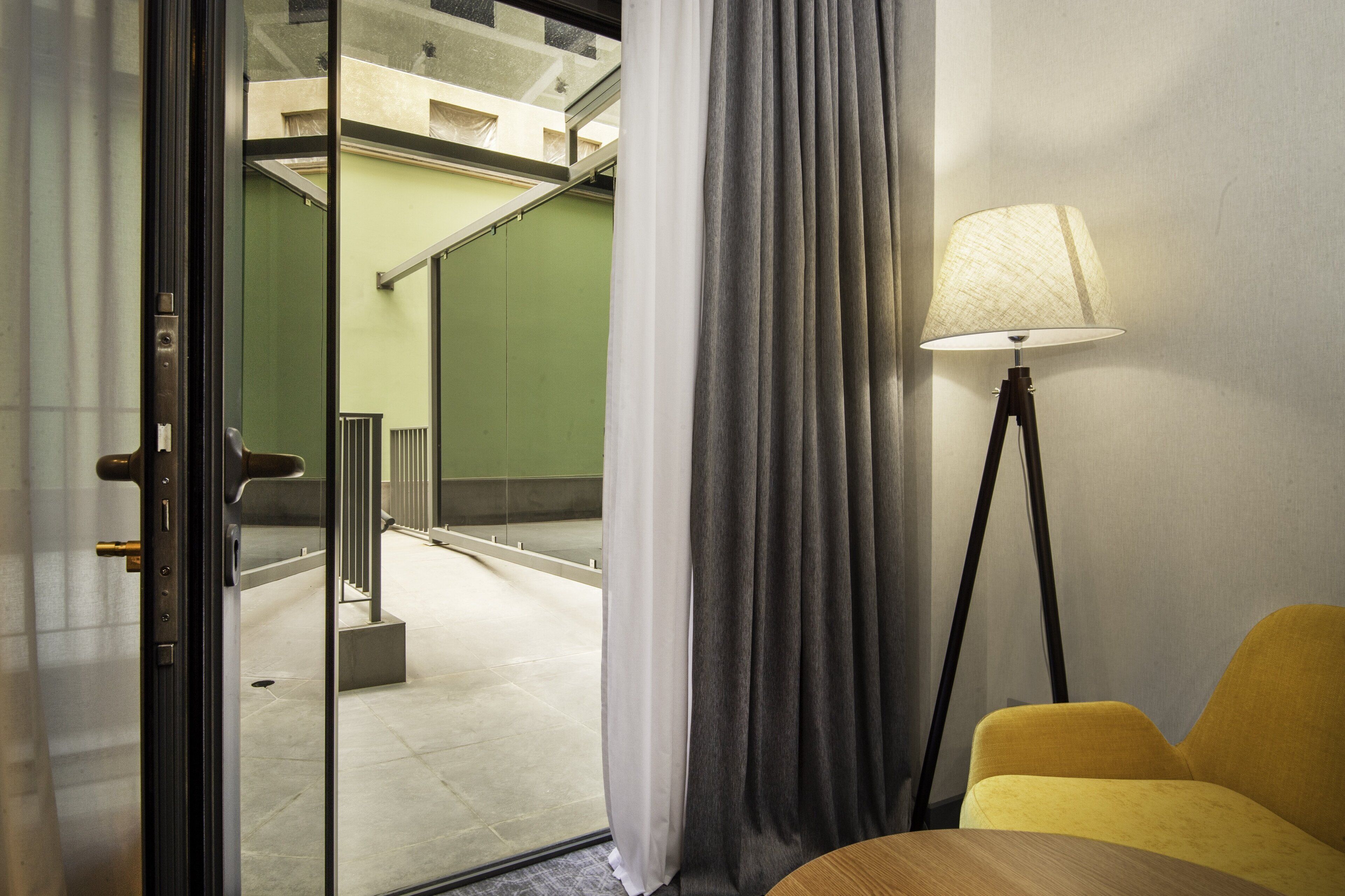 A hotel room with a glass door, a lamp, and a yellow chair.