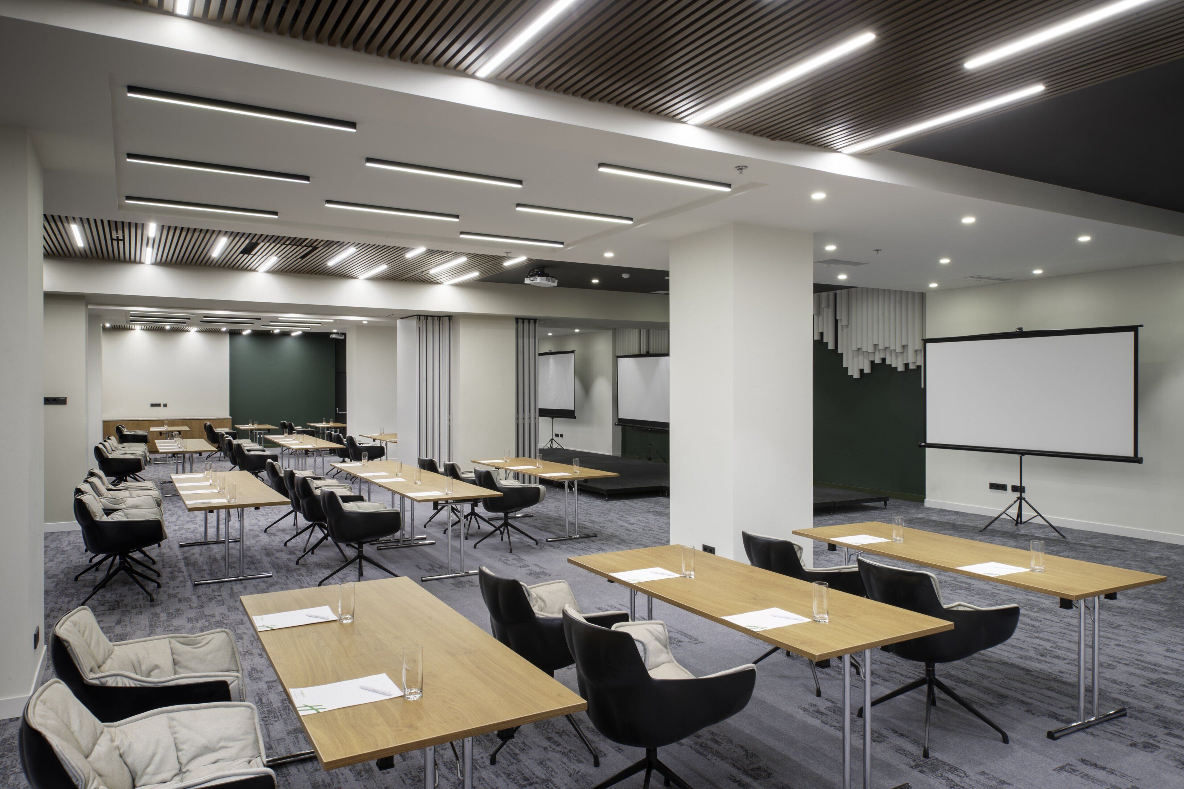 Uma sala de conferências com várias mesas e cadeiras, uma tela de projetor e um quadro branco.