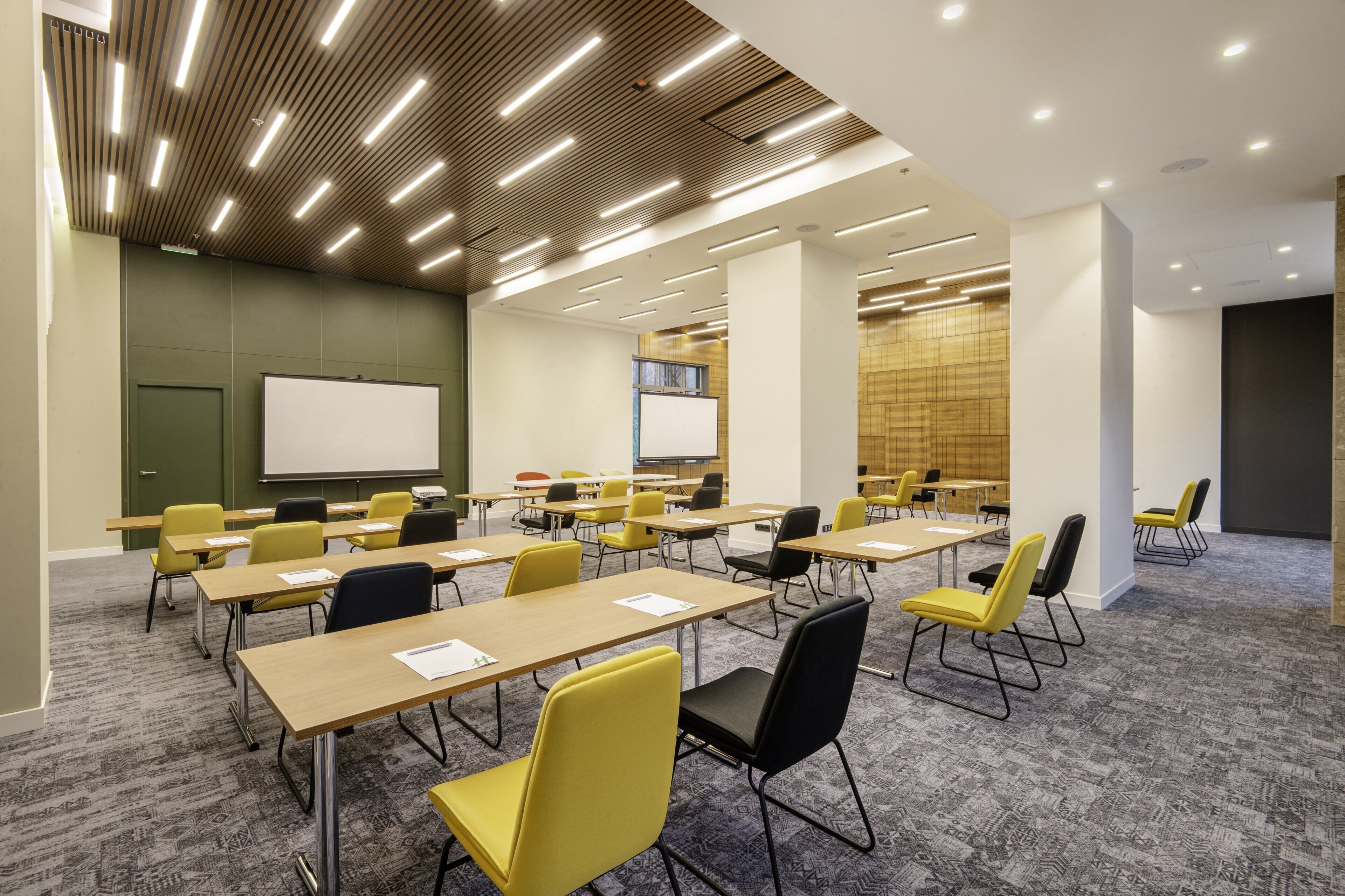 Una sala conferenze con diversi tavoli e sedie, una lavagna e uno schermo per proiettore.