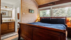 A bedroom with a wooden bed, a large window, a wooden ceiling, and a bathroom with a wooden vanity. - Dog friendly at the Seventh Mountain Resort! (Bend)