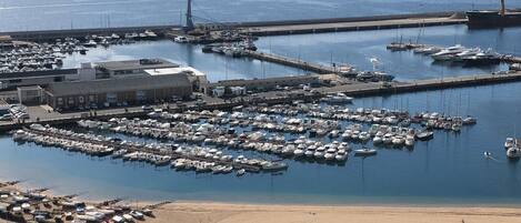Uma marina com vários barcos atracados, uma praia de areia e um estacionamento com carros.