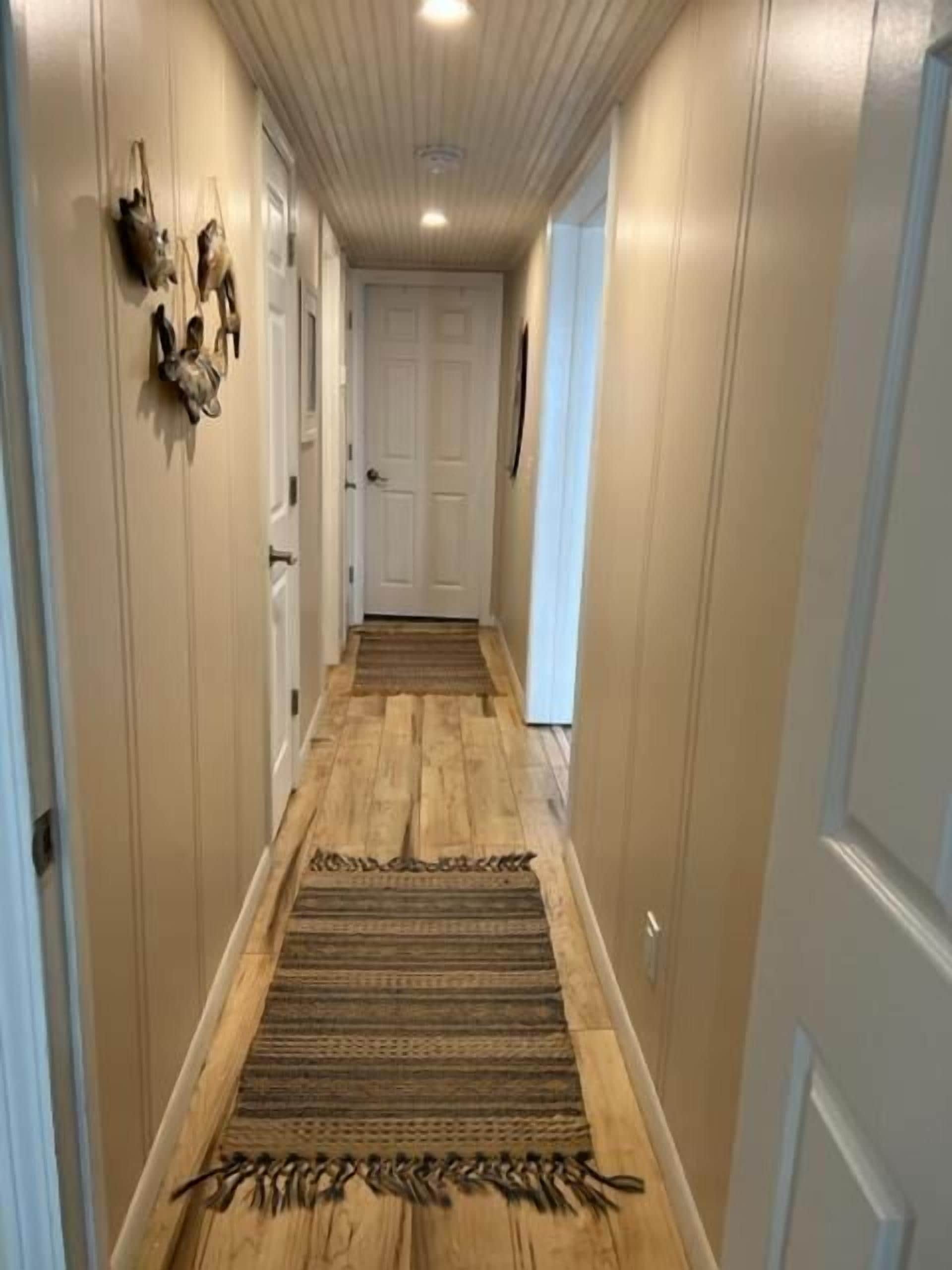 Un couloir doté d’un plancher en bois, d’un tapis à motifs et d’œuvres d’art décoratives accrochées aux murs.