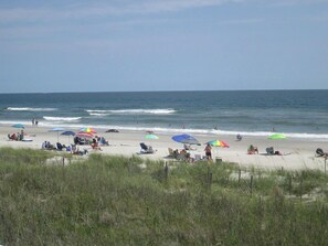 A beach with people relaxing under colorful umbrellas, some sitting on beach chairs, and others standing.