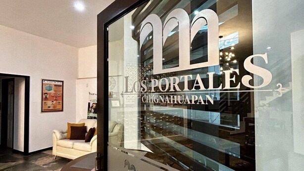 Een modern interieur met een glazen deur waarop de tekst 'Los Portales' staat, een witte bank en een vloer met een patroon.