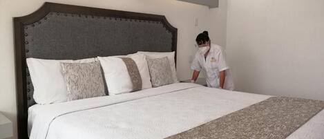 A neatly made bed with a patterned bedspread and pillows, a wooden headboard, and a white wall with a light fixture.