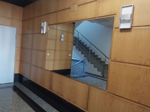 A corridor with wooden panel walls, a mirrored section reflecting a staircase, and a door on the left.